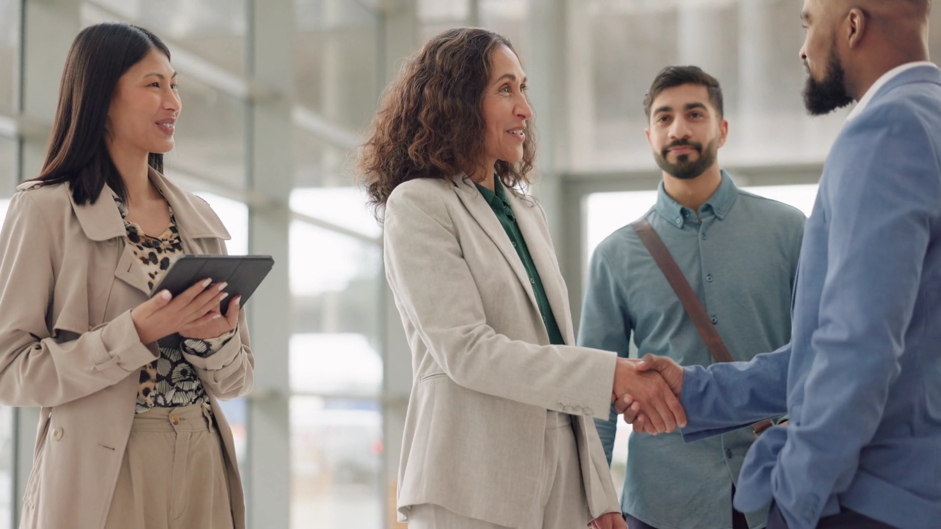 A woman shaking hands with another man in front of two other men.